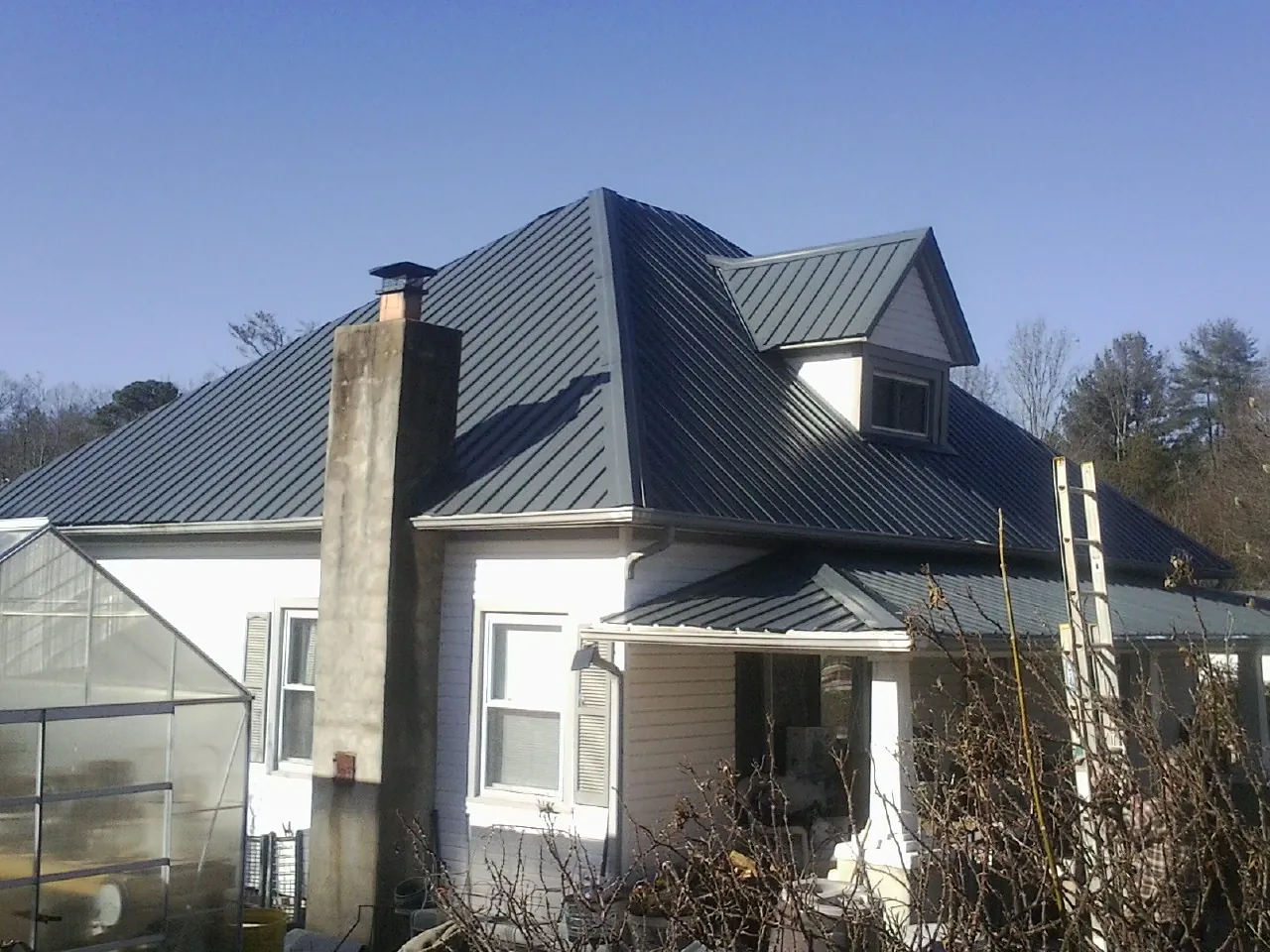 Dark blue standing seam metal roof on a white farmhouse with dormer — Slate & Tile Roof Repair by Roofing Brothers in Southold