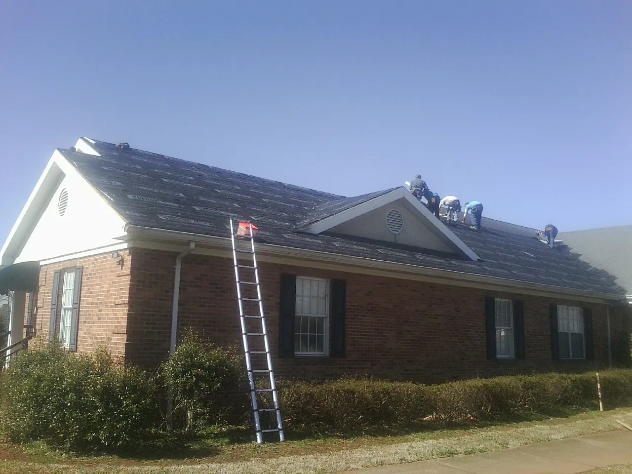 Crew tearing shingles off a brick ranch roof with a ladder set — Metal Roof Repair work by our crew in Southold