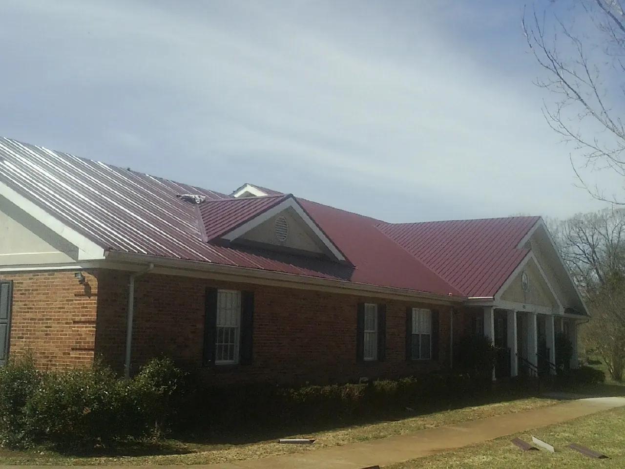 Red metal roof with gabled entries on a long brick building, from a Hail Damage Roof Repair job in Southold