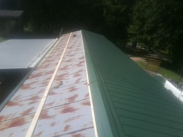 Old rusted panels beside newly installed green metal roofing — Wind Damage Roof Repair by Roofing Brothers in Southold