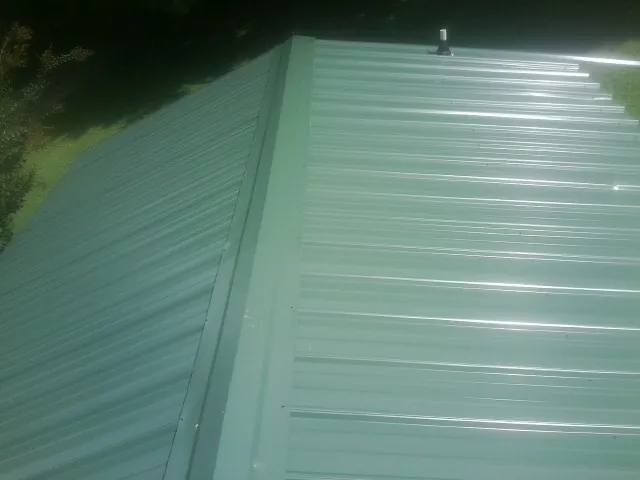 New green metal panels meeting at the ridge of a roof — Flat Roof Repair work by our crew in Southold