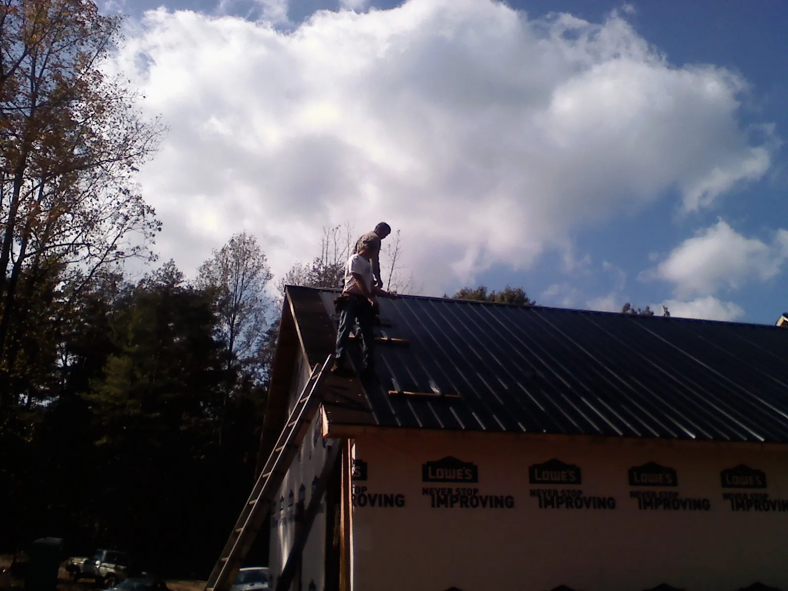 Roofer fastening dark metal panels high against a cloudy sky, from a Roof Inspection job in Southold