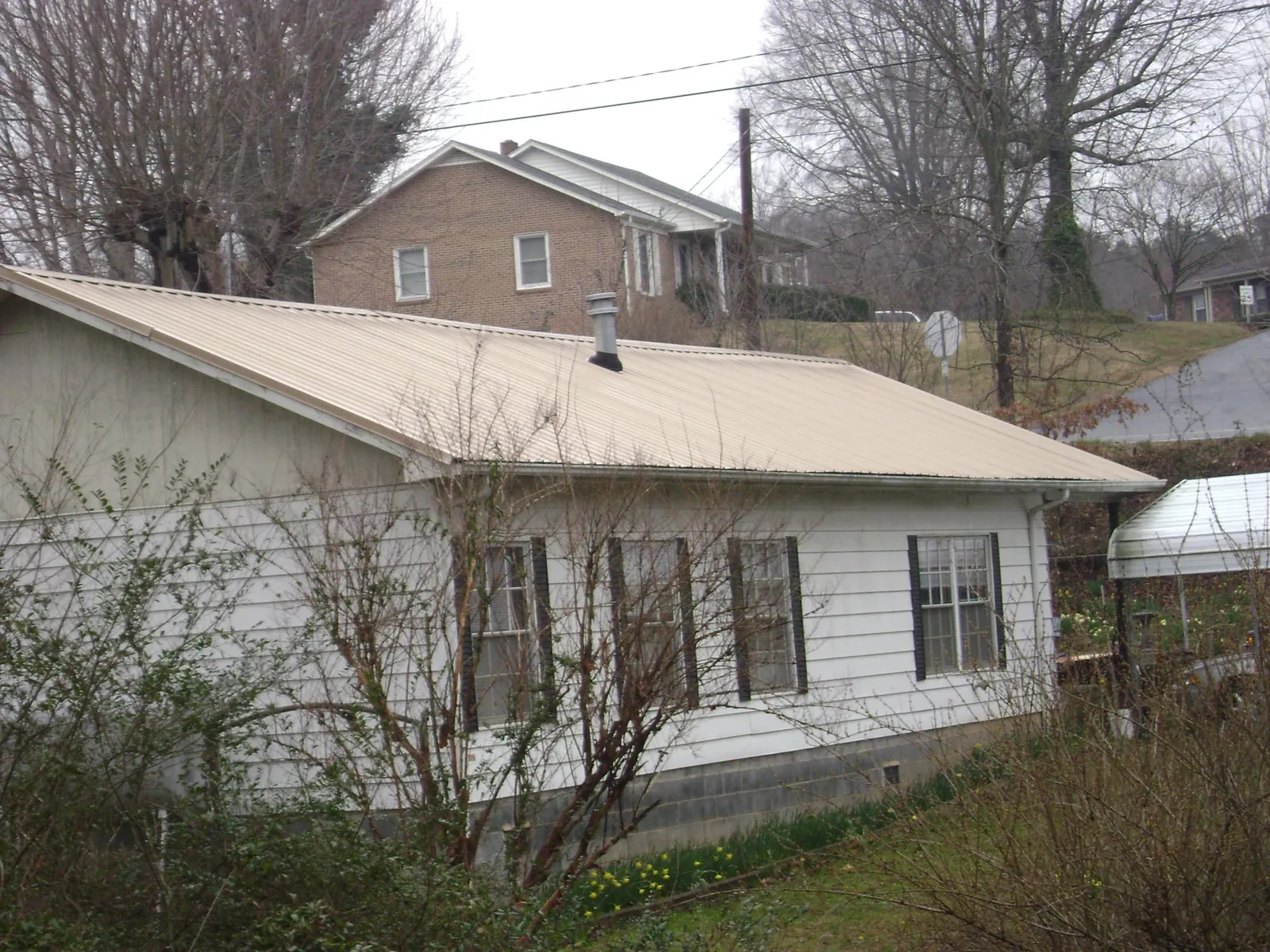 Tan metal roof on a white sided house set into a hillside — Commercial Roofing by Roofing Brothers in Southold
